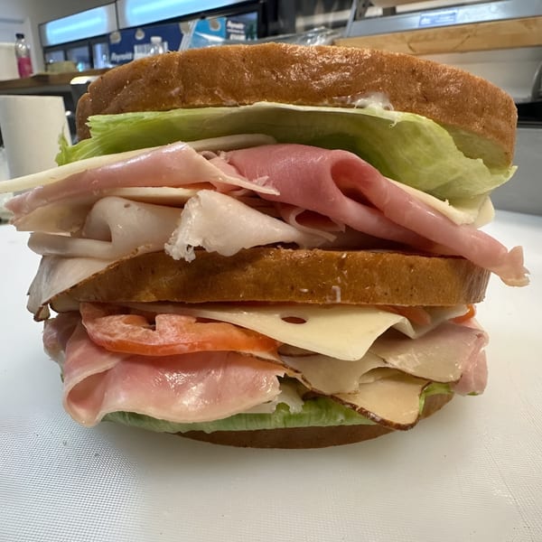 A towering deli sandwich from Koch's Deli, packed with various meats, cheese, lettuce, and tomato.