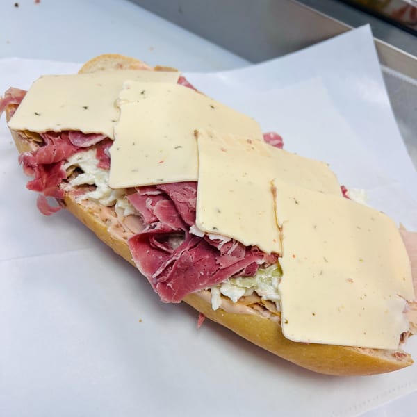 A large deli sandwich from Koch's Deli, filled with meat, cheese, and coleslaw on a white paper.